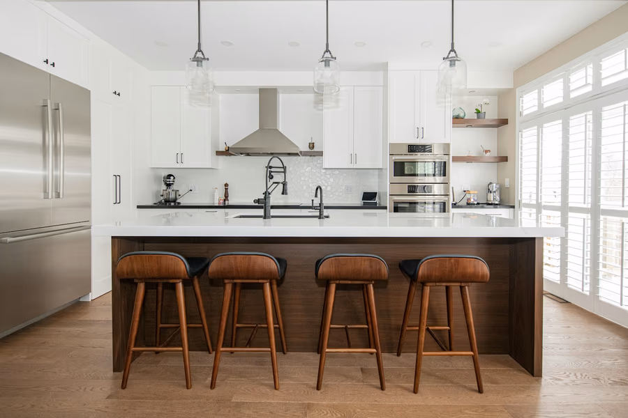 A kitchen island with four bar stools tucked under a countertop overhang, with a clear aisle between the island and the perimeter cabinet run behind it