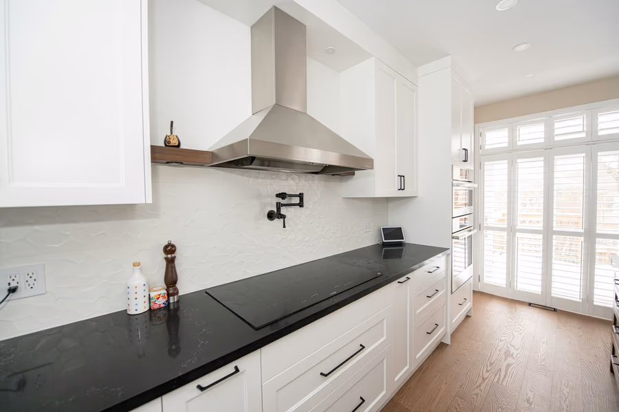 A stainless steel wall-mounted chimney range hood above a cooktop, with the duct concealed in a boxed enclosure running up to the ceiling
